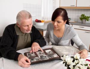 Eine junge Frau schaut mit Senioren ein Fotoalbum an